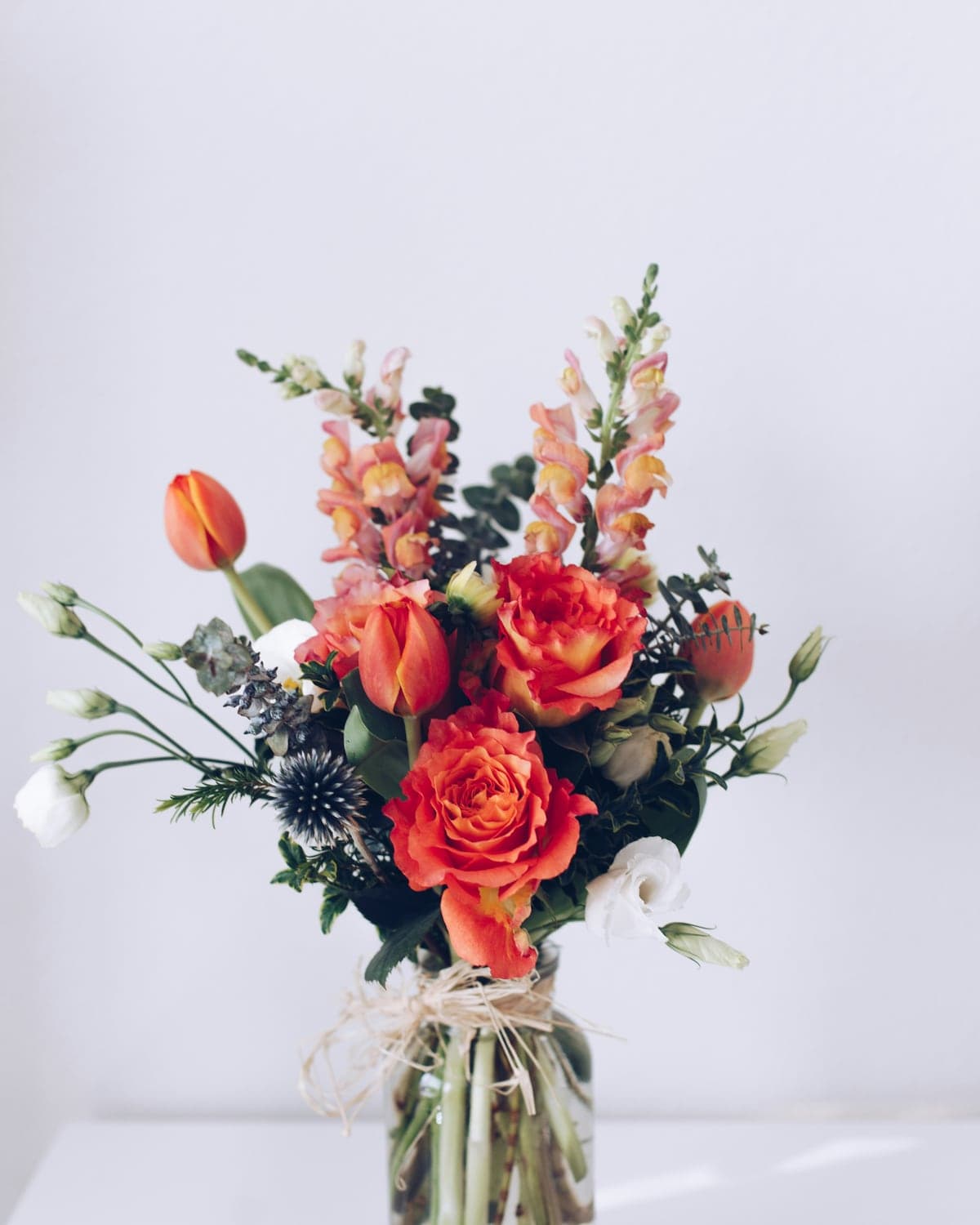 Coral roses and orange snapdragons arranged in a glass vase