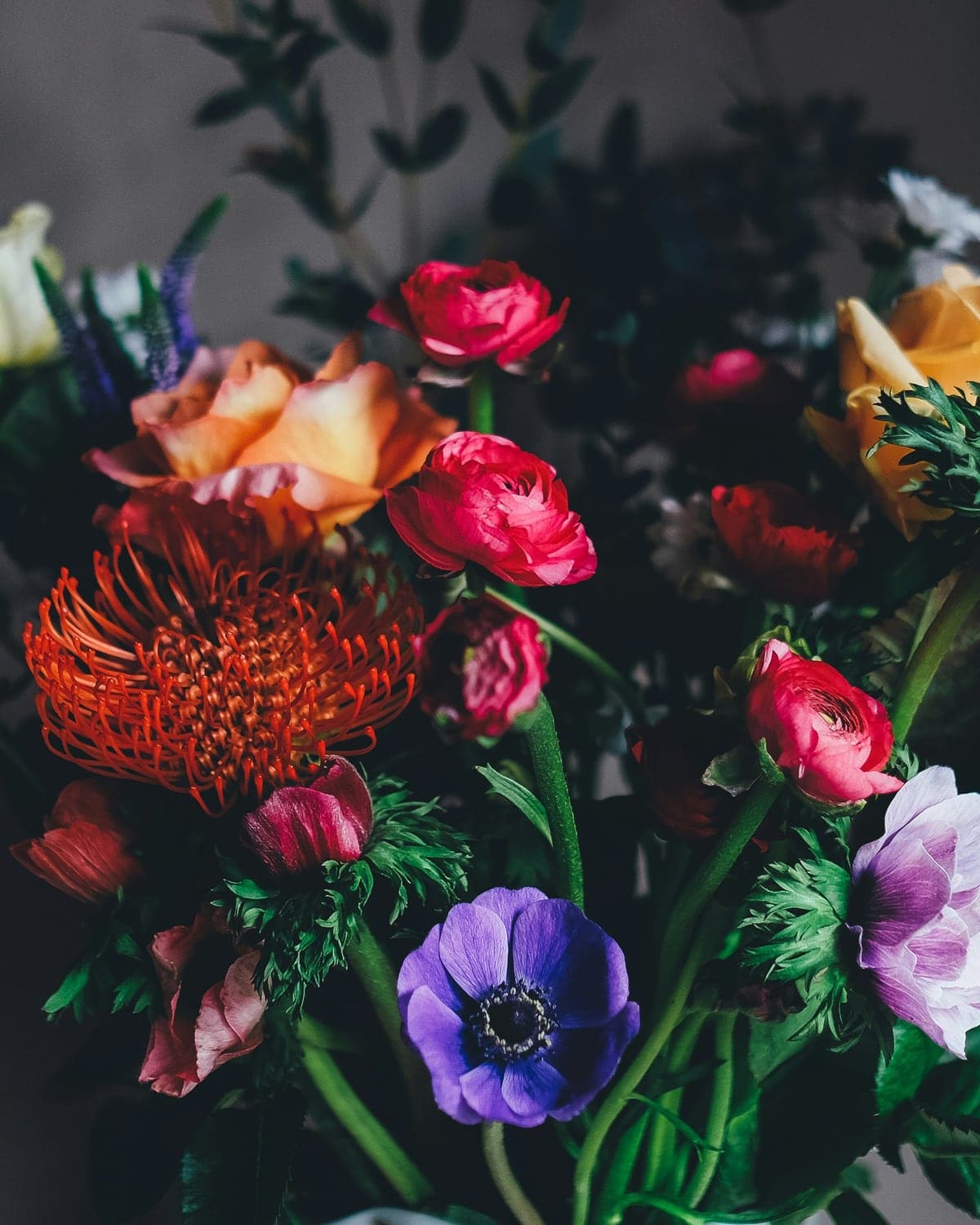 A dark arrangement of anemones, protea and deep red ranunculus