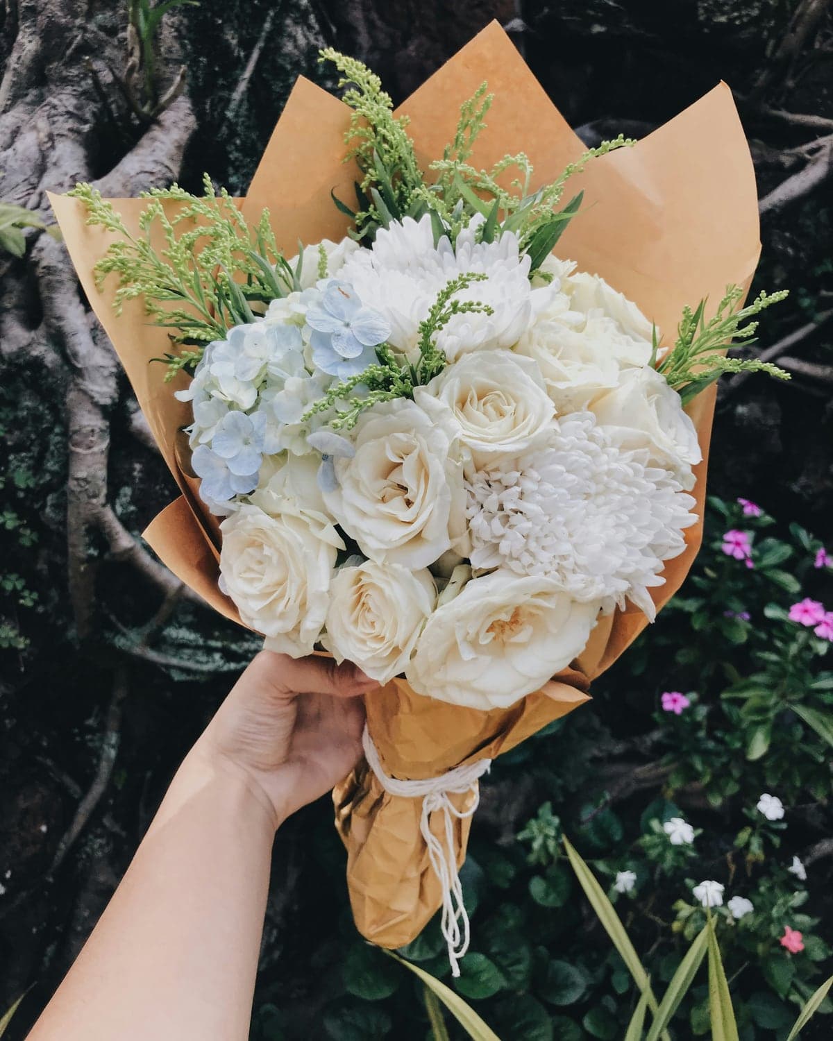 A cream and white bouquet of roses and hydrangea in kraft paper
